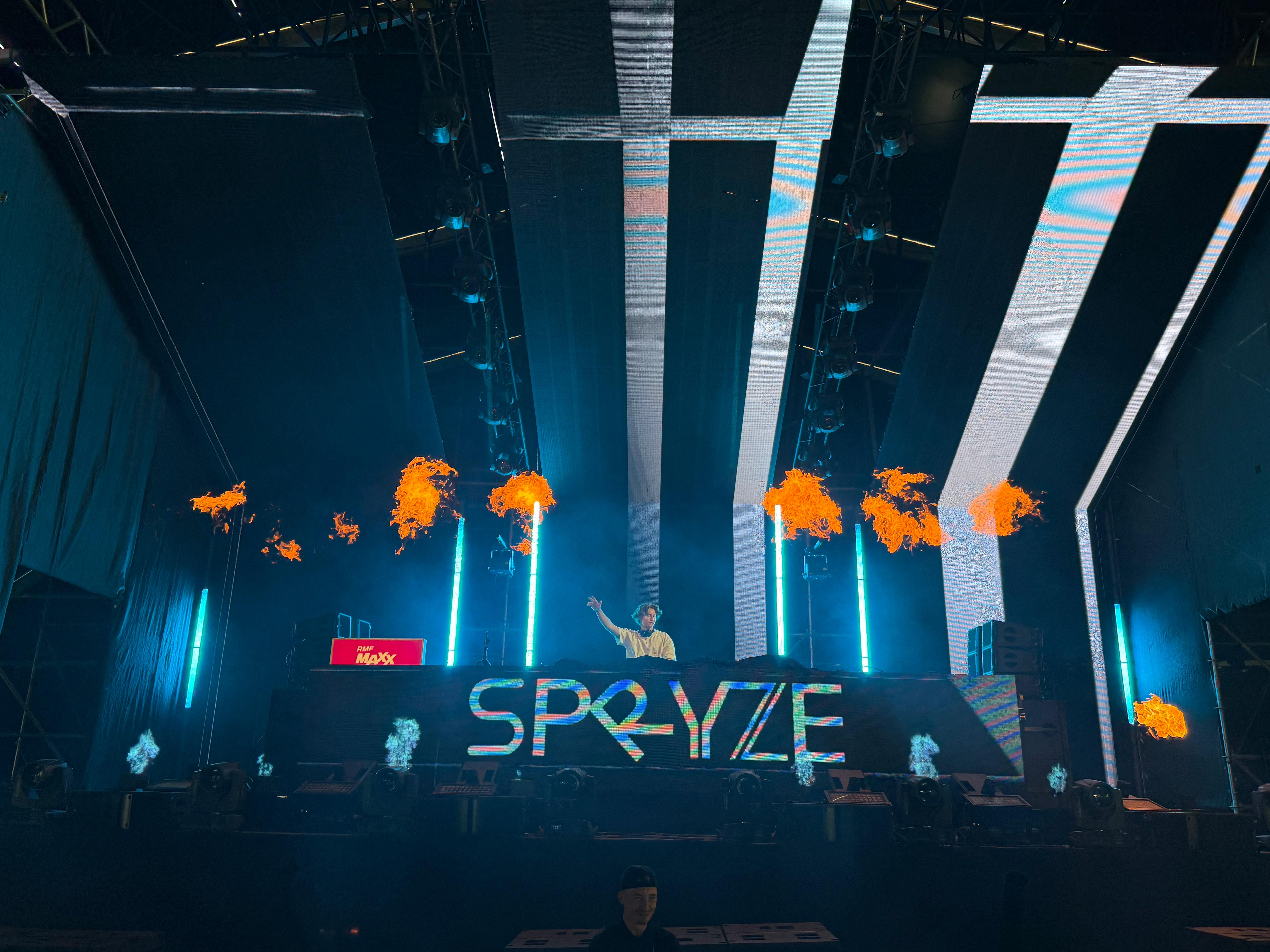 Spryze performing on a festival stage with flames and LED screens